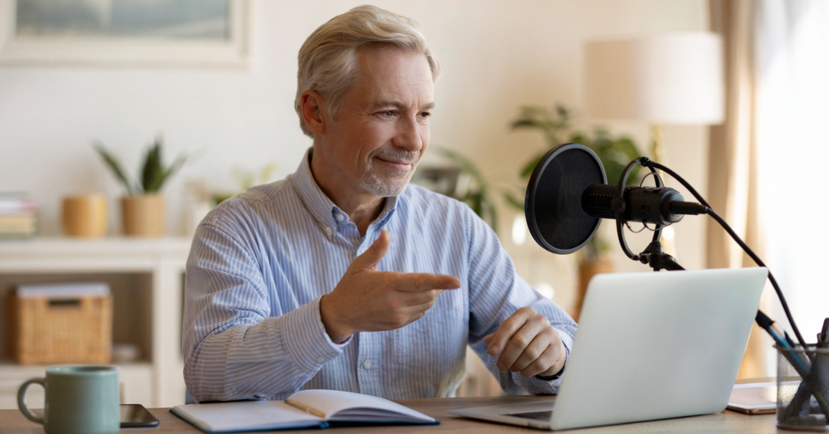 Retired man recording an online course at home using a laptop and microphone.