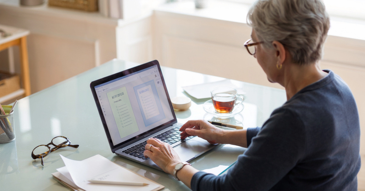 A retired person creating simple digital products on a laptop, such as printables and mini-guides, at a bright home desk.