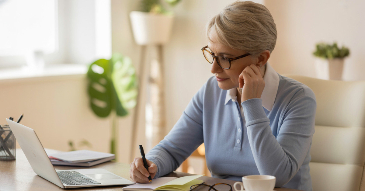 Retiree taking notes at a laptop, preparing to start coaching online with confidence.