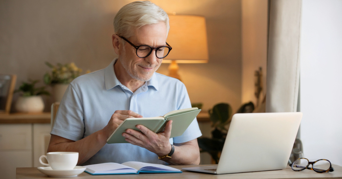 A retired person smiling with a sense of accomplishment while closing a notebook or looking at a laptop after learning about digital products.